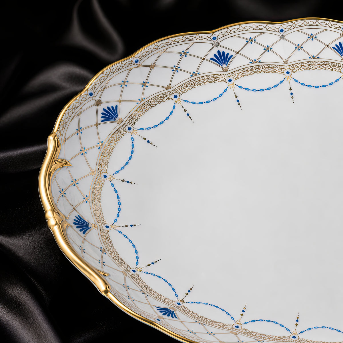 Close-up of the Valesse Azure oval platter showing the sculpted gold edge, blue motifs and intricate lattice border.